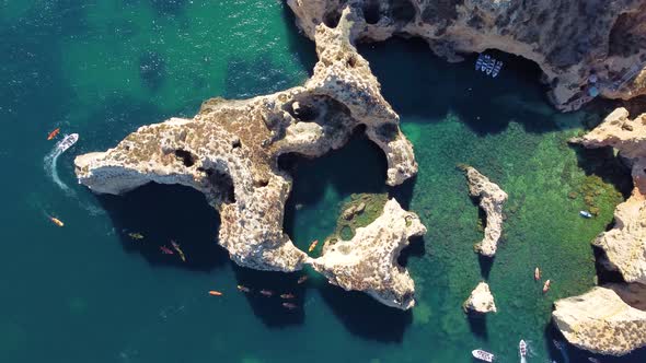 Drone shot of kayaks and boats passing in the ocean, people exploring caves and tunnels.