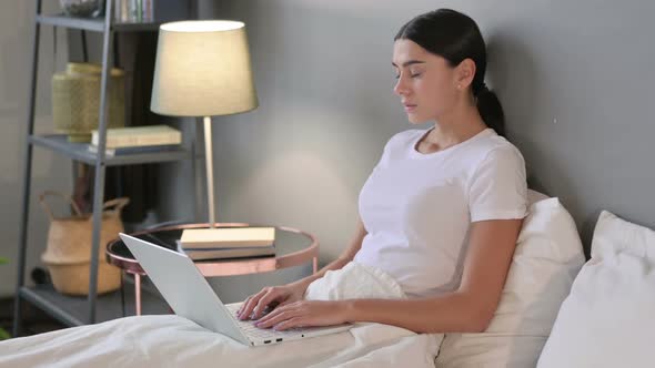 Drowsy Latin Woman with Laptop Falling Asleep in Bed