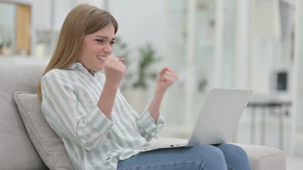 Excited Young Woman Celebrating Success on Laptop at Home