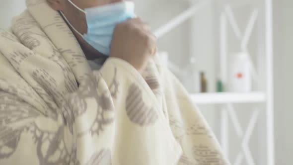 Close-up of Coughing African American Man in Face Mask Wrapped in Blanket. Portrait of Ill Exhausted