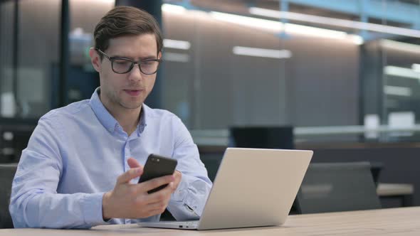 Young Man with Laptop Using Smartphone