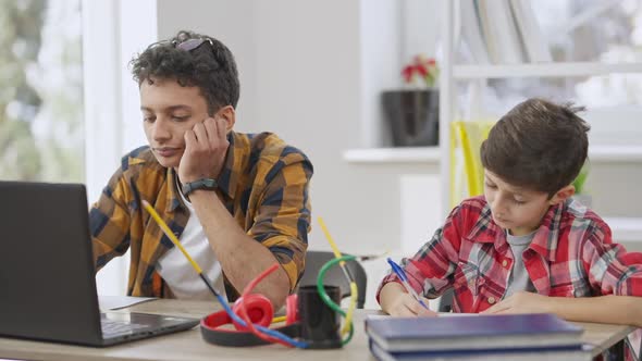 Portrait of Concentrated Teen and Little Students Doing Homework Indoors Sitting at Table