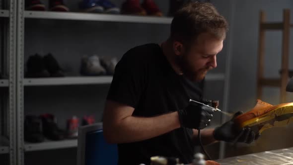 Tracking Shot of Professional Shoemaker in Black Latex Spraying Paint of Light Brown Leather Shoes