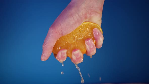 Female Hand Squeezing an Orange on a Blue Background