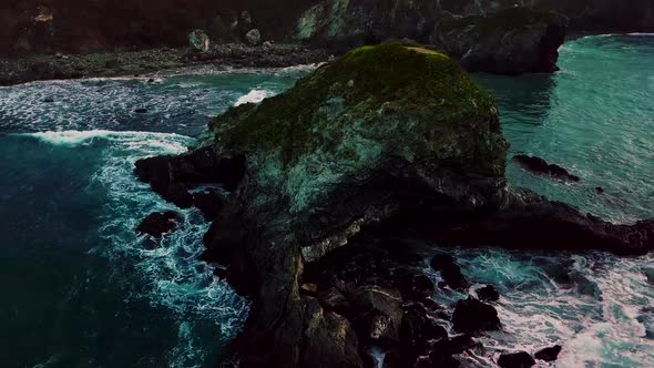 Rising aerial shot of a cave carved into ocean rock by crashing waves at Sand Dollar Beach in Big Su