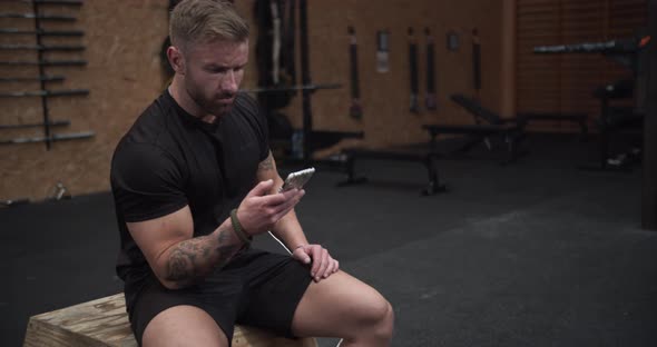 Athletic Man Sitting on a Wooden Stool While Looking at His Phone