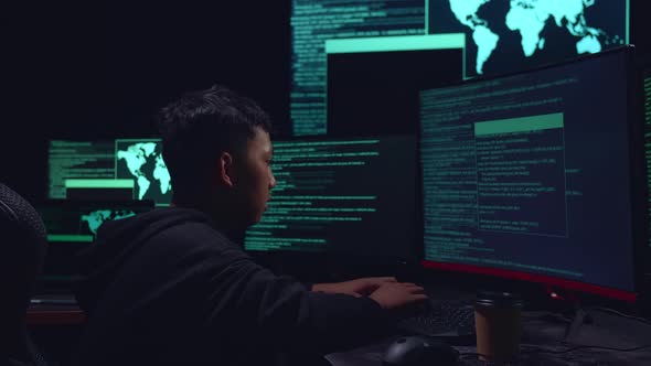 Asian Boy Hacker Hacking With Multiple Computer Screens In Dark Room