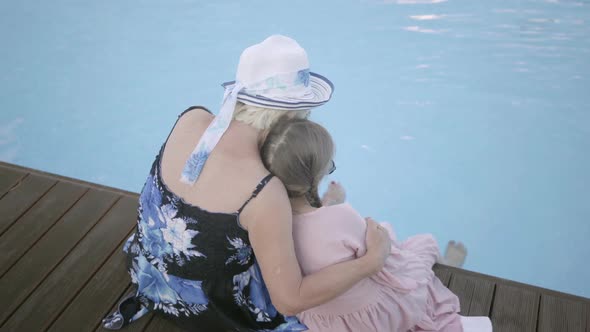 Back View of Little Funny Girl with Pigtails and Mature Woman Sitting on the Edge of the Pool