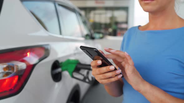 Woman Using Smartphone While Her Car Is Refueling