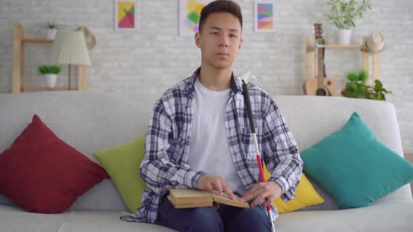 Portrait Blind Asian Young Man Reading a Book of Braille Text Sitting on the Couch in the Living