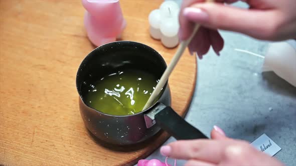 Hand made candles production, female hand mixing melting wax in a pot. Slow motion