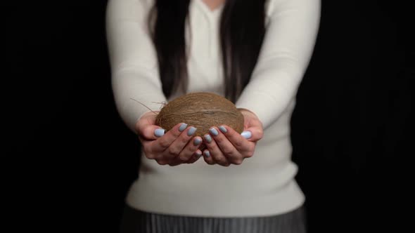 Woman Shows Coconut in Hands on a Black Background