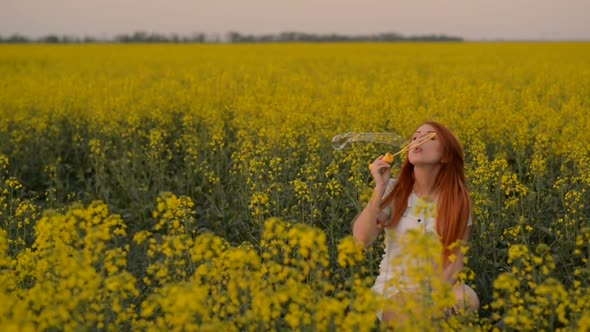 Young Redhair Woman Blowing Bubbles at the Camera Outdoors in Summer Meadow