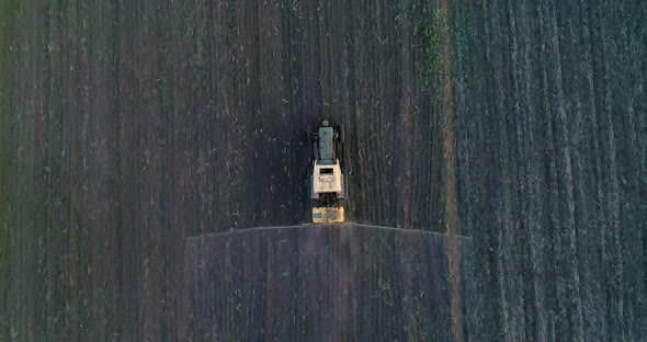 Tractor with trailed sprayer spraying chemicals on agricultural field. Aerial view.