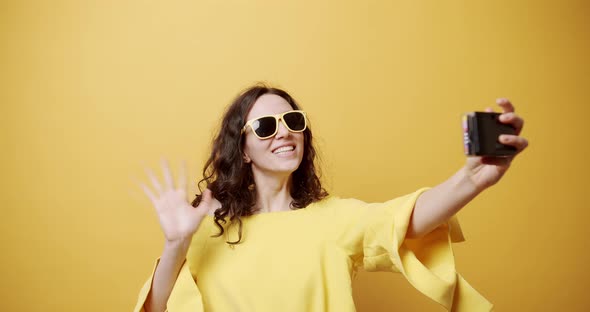 A Young Girl Smiles Takes a Picture with the Retro Camera on a Yellow Background