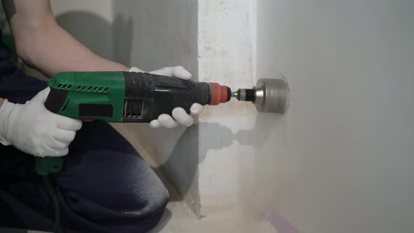 A Construction Worker Using a Drill Puncher Makes a Hole in the Wall for the Electrician Crowning on