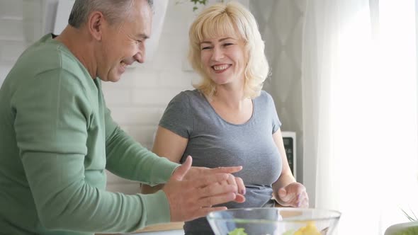 Retired Husband and Female Pensioner Dancing in Kitchen During Salad Preparing