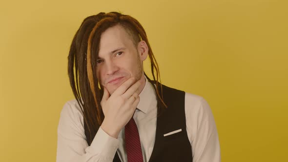 Young Happy Man Looking at Camera and Scratching Chin on Yellow Background