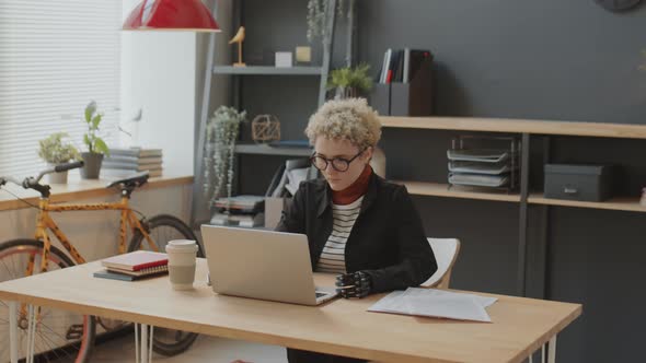 Woman with Prosthetic Arm Working on Laptop in Office