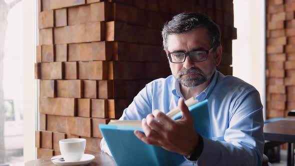 Happy Handsome Senior Man Reading a Book in Cafe