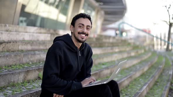 Man Using Laptop and Smiling at Camera