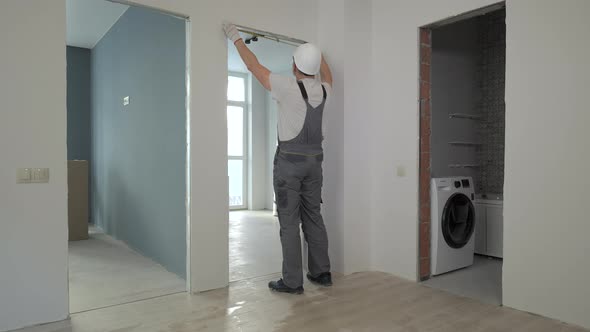 A Builder in Working Uniform Checks the Size and Quality of Doorways in a New Apartment