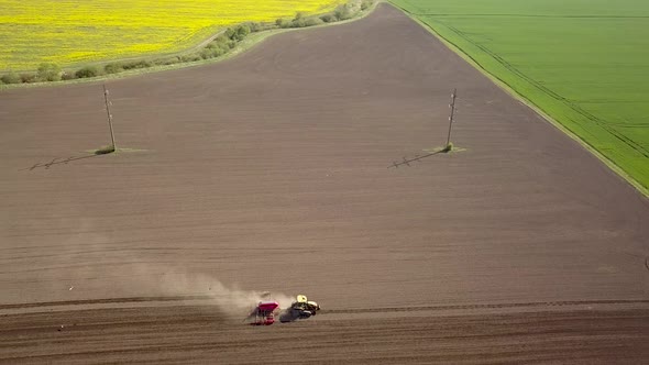 Top down aerial view of green tractor cultivating ground and seeding a dry field. Farmer preparing 