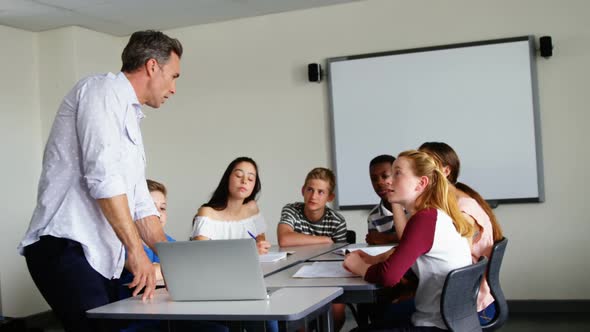 Teacher assisting schoolkids on laptop