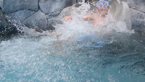 A boy plays on a waterslide water slide in a pool at a hotel resort.