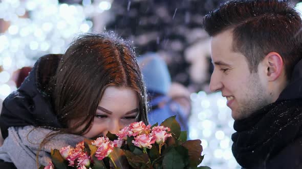 Close-up Man Gives a Gift To a Woman on the Street Decorated with Lights and Garlands, New Year and