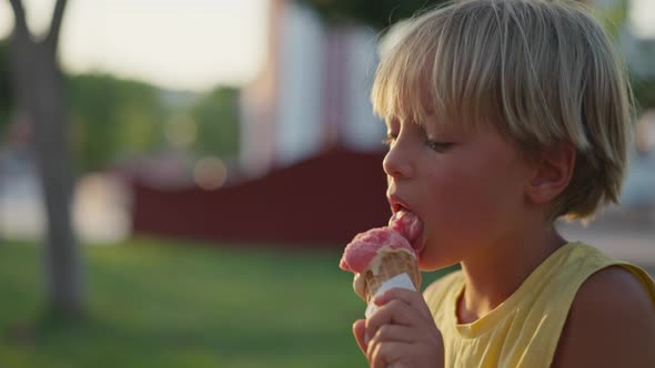 Outdoor Portrait of Young Caucasian Boy with Blond Hair Eating Ice Cream in Crispy Cone