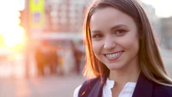 Young Attractive Girl in the Evening Urban Landscape, Smiles, Looking to the Camera