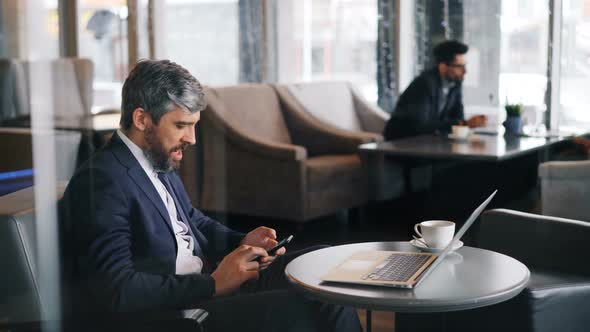 Tired Businessman Using Smartphone in Cafe Touching Screen and Yawning