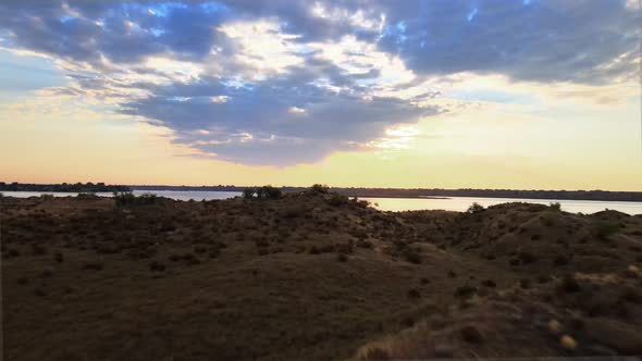 Rising up over scrubland revealing a pristine lake reflecting golden sunrise, aerial