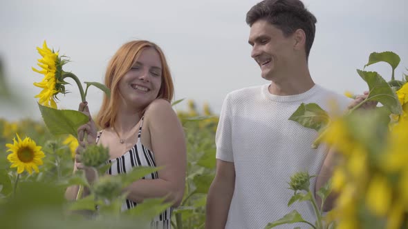 Portrait of Happy Couple Laughing and Covering Their Faces with the Big Sunflower on the Sunflower