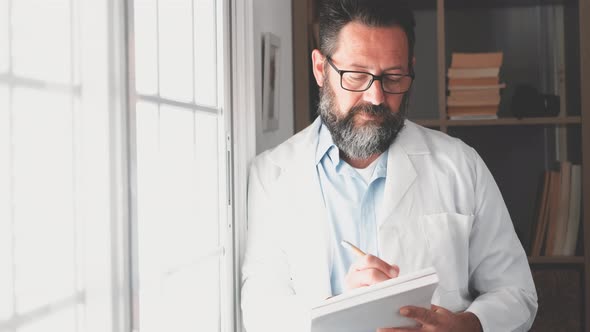 Pensive young male caucasian doctor in white medical uniform look in window