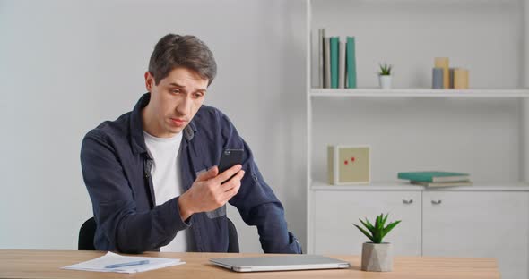 Caucasian Millennial Business Man Adult Young Guy Entrepreneur Sitting in Office Home Holding Phone