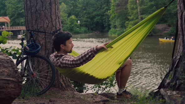 A Young Caucasian Man Relaxing in a Hammock After Riding His Bicycle in the Woods By the Lake