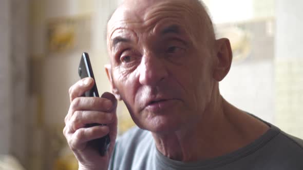 Cheerful Caucasian pensioner over 70 communicates cheerfully on the phone. Elderly man with dementia