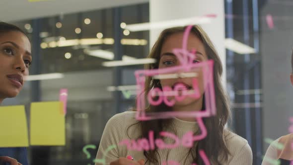 Diverse group of female work colleagues brainstorming writing notes on glass wall