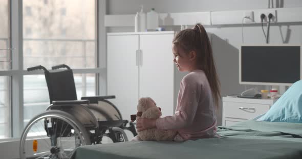 Cute Happy Child Alone in Hospital Room Sitting on Bed with Teddy Bear