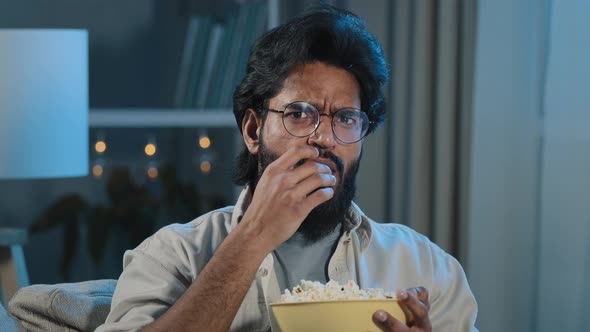 Interested Attentive Arabic Hispanic Indian Bearded Man Guy in Glasses Eating Popcorn Watching TV