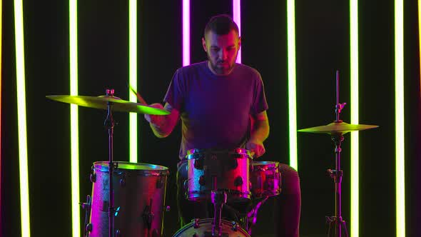 The Talented Drummer Performs a Drum Solo in the Studio Against a Background of Bright Neon Lights
