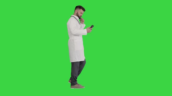 Male Doctor in White Medical Uniform Walking and Using Smartphone on a Green Screen, Chroma Key.