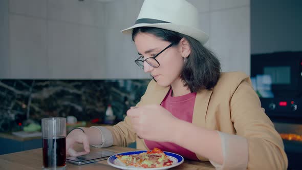 Teenage Brunette Girl in Hat and Glasses Eating and Browsing Mobile App