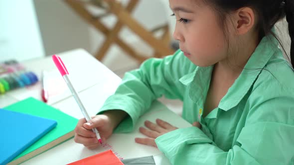 Asian girl sitting at table writing in school book