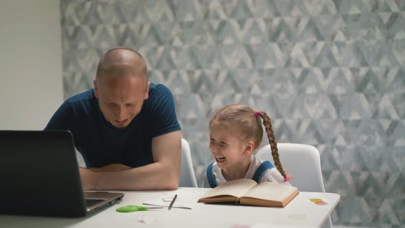 Young Dad and Little Daughter Laugh at White Table in Room