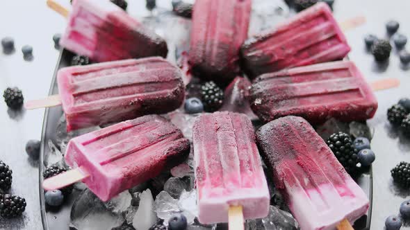 Homemade Fresh Frozen Blueberry and Blackberry Popsicles on Black Plate with Ice Sitting on Stone