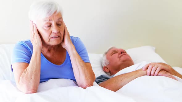 Irritated woman covering her ears while man snoring on bed