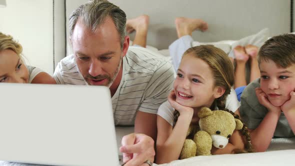 Family using laptop while lying together in bedroom at home 4k